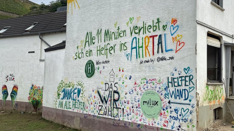 Auf einer Hauswand in Dernau steht der Spruch: "Alle elf Minuten verliebt sich ein Helfer ins Ahrtal".  (Foto: SWR)