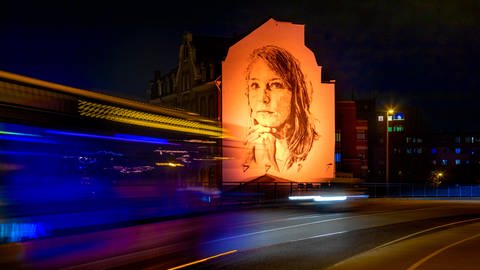 Auch das Bild einer jungen Frau auf einer Hauswand an der Balduinbrücke in Koblenz wird wie schon 2020 wieder in oranges Licht getaucht - als sichtbarer Protest gegen Gewalt an Frauen. (Foto: orangetheworld/Ulli Piel)