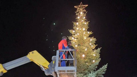 Zwei Männer in einer Kran hängen eine Lichterkette an einem Weihnachtsbaum auf, der mitten im flutgeschädigten Ort Schuld an der Ahr steht. Er soll ein Zeichen der Hoffnung sein.  (Foto: SWR)