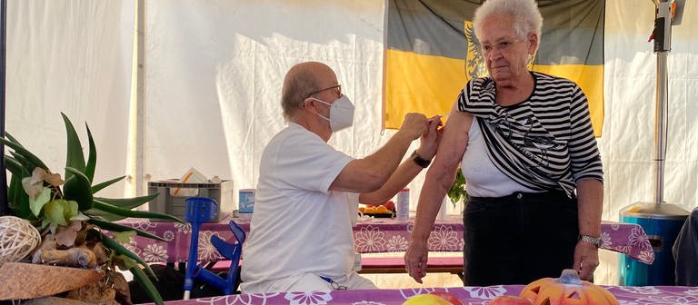 Ein Arzt in einem Zelt der Essensausgabe impft eine ältere Dame. (Foto: SWR)