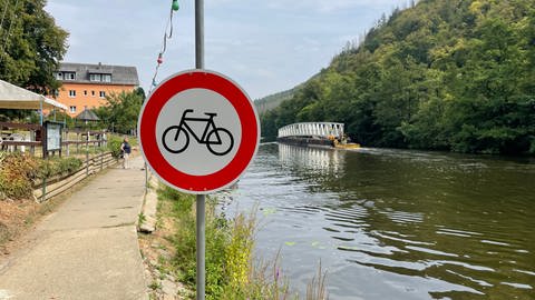 Radfahren verboten Schild, im Hintergrund eine Brücke, die über die Lahn auf einem Ponton gezogen wird. (Foto: SWR)