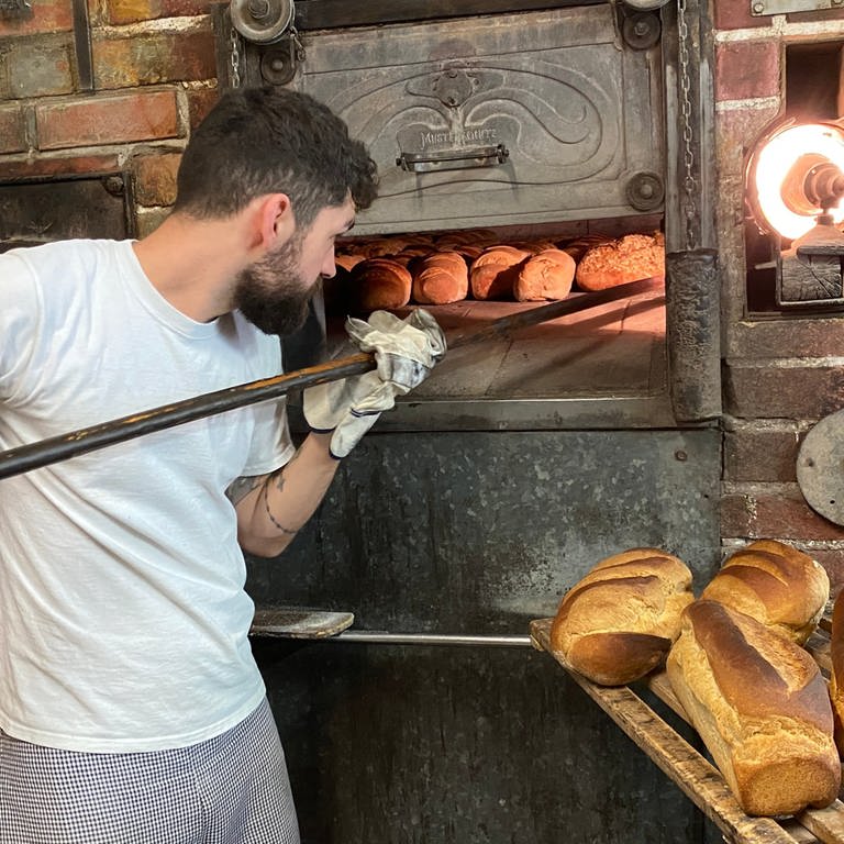 Ein junger Bäcker schiebt Brotlaibe in seinen Holzofen (Foto: SWR)