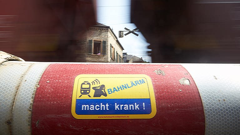 Ein Güterzug fährt am Mittelrhein unmittelbar an Wohnhäusern und an einer Schranke mit der Aufschrift "Bahnlärm macht krank" vorbei.  (Foto: picture-alliance / Reportdienste, Picture Alliance)