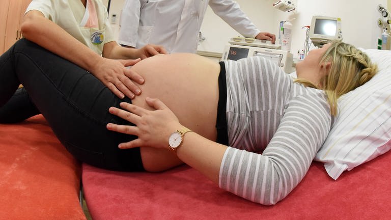 Eine schwangere Frau liegt im Krankenhaus auf einer Liege und wird von einer Hebamme und einem Arzt untersucht (Foto: picture-alliance / Reportdienste, picture alliance / Waltraud Grubitzsch/dpa-Zentralbild/dpa)