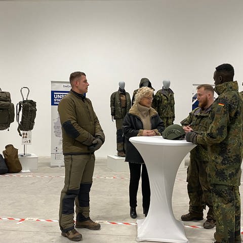Bundesverteidigungsministerin Lambrecht steht im Bekleidungszentrum der Bundeswehr in Simmern zusammen mit Soldaten an einem Tisch.  (Foto: SWR, Christian Giese-Kessler )