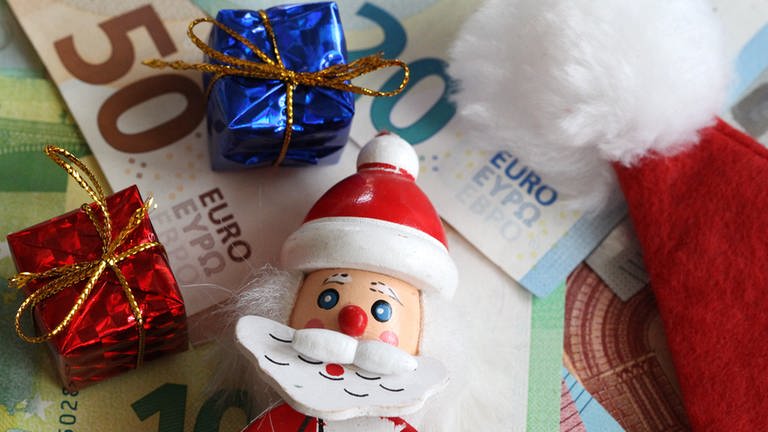 Weihnachtsmannfigur und kleine Geschenke liegen auf Geldscheinen (Foto: picture-alliance / Reportdienste, Fleig / Eibner-Pressefoto)