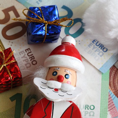 Weihnachtsmannfigur und kleine Geschenke liegen auf Geldscheinen (Foto: picture-alliance / Reportdienste, Fleig / Eibner-Pressefoto)
