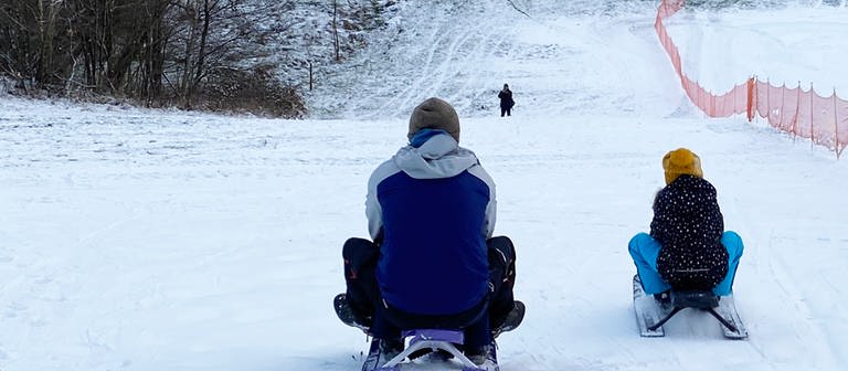 Rodel-Spaß bei Kirburg im Westerwald. Vater und Kind von hinten auf Schlitten im Schnee (Foto: SWR)