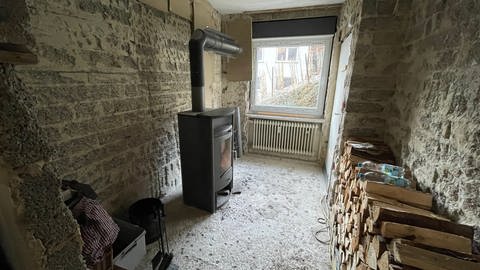 Ein Holzofen und ein Stapel mit Holzscheiten stehen in einem entkernten Zimmer (Foto: SWR)