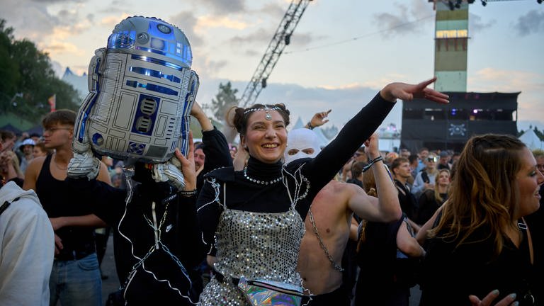 Nature One 2023: Techno-Fans halten eine Attrappe des Roboters R2D2 aus Star Wars vor der Bühne hoch.