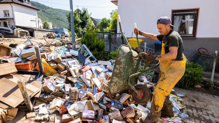 Ein Helfer schüttet mit einer Schubkarre vom Waser beschädigte Bücher auf einen großen Müllhaufen mit Sperrmüll
