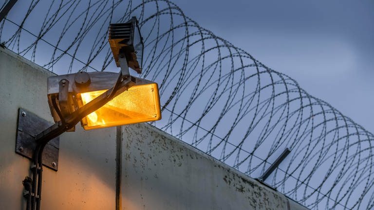 Stacheldraht über einer Gefängnismauer bei Dämmerung (Foto: picture-alliance / Reportdienste, Schoening)