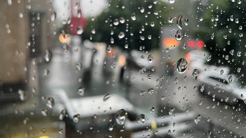 Regentropfen laufen an einer Fensterscheibe herunter, dahinter sieht man verschwommen eine verregnete Straße (Foto: SWR)