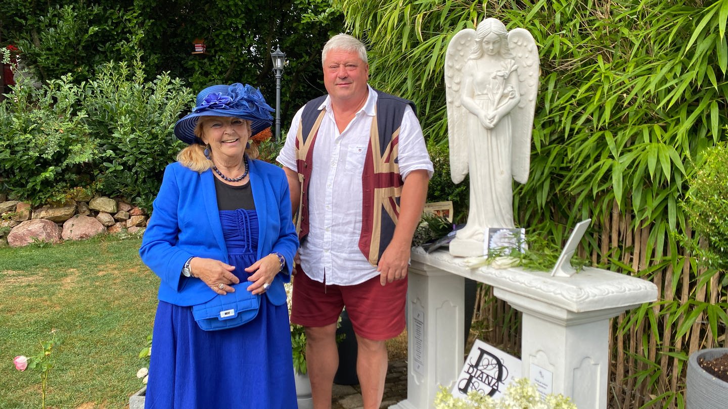 Eine Frau und ein Mann stehen in einem Garten neben einer Engelsfigur. Die Gedenkstatue soll an den Tod der verstorbenen Lady Di erinnern. (Foto: SWR)