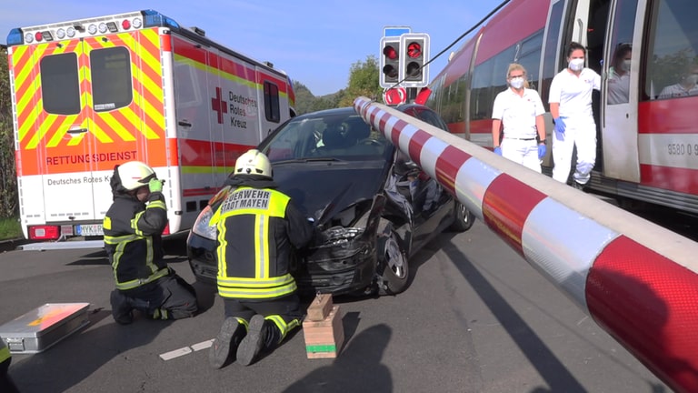 Unfall am beschrankten Bahnübergang: Ein Rettungswagen und Helfer an einem Pkw, die Schranke ist geschlossen und ein Zug steht (Foto: Winkler)
