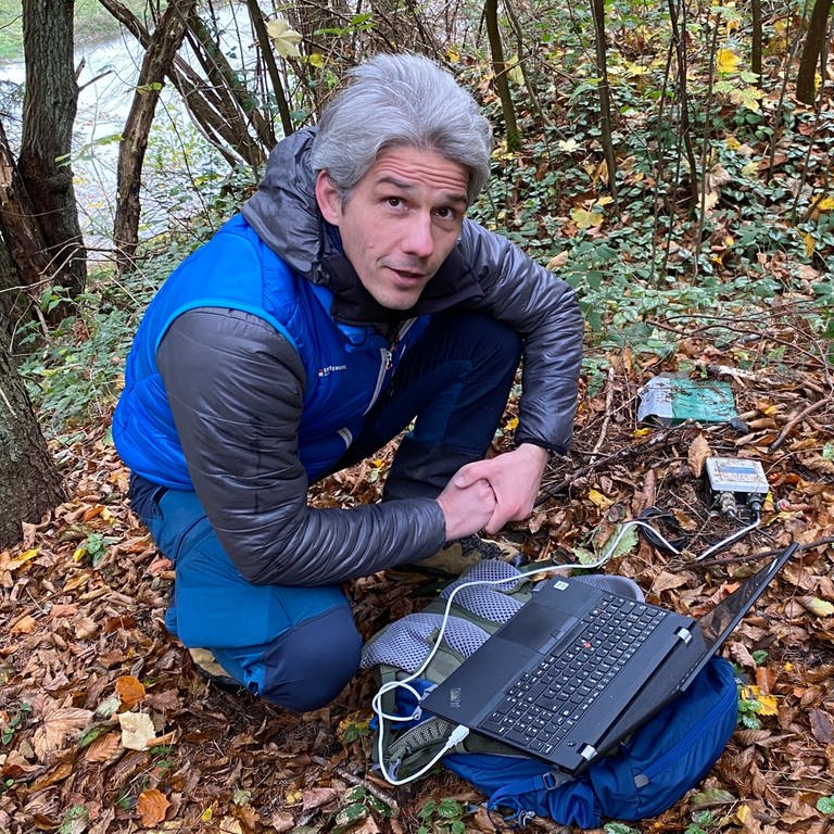 Der Geograph Rainer Bell hockt mit Laptop am Boden, der mit Laub bedeckt ist. (Foto: SWR)