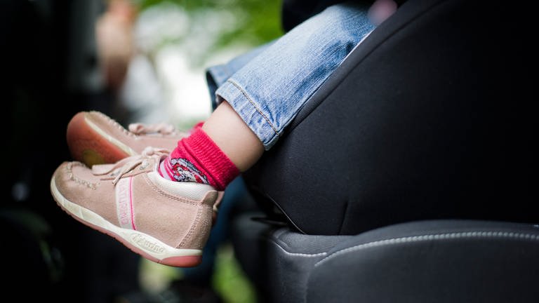 Ein Kleinkind mit braunen Schuhen und roten Socken sitzt im Autositz. Man sieht den Fußbereich und den unteren Teil des Sitzes. (Foto: picture-alliance / Reportdienste, Nicolas Armer)