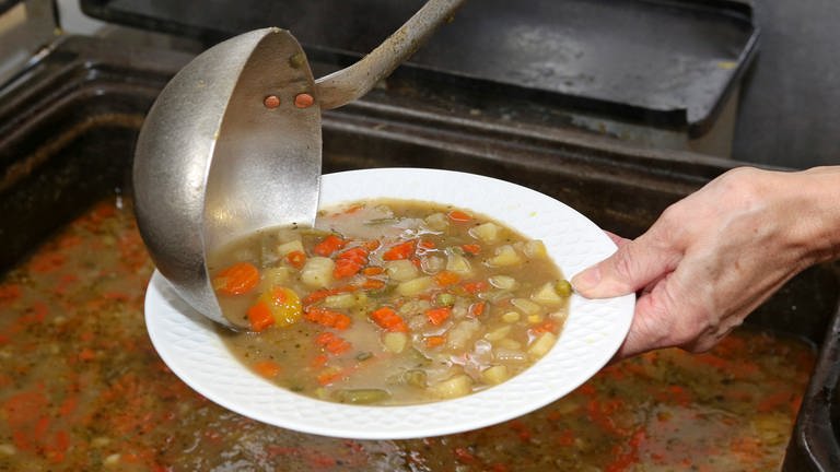 Eine Hand hält einen Teller mit Suppe