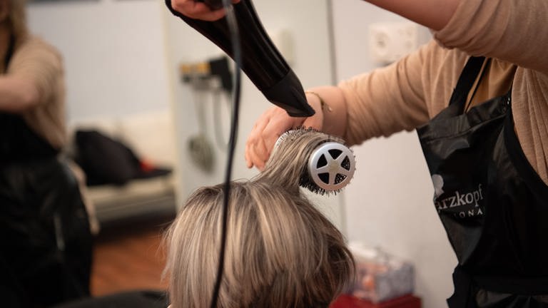 Eine Friseurin föhnt einer Frau die Haare