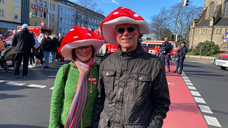 Ein Mann und eine Frau lachen mit rot-weißen Pilzkopf-Hüten beim Rosenmontagszug 2023 in Koblenz in die Kamera. (Foto: SWR)