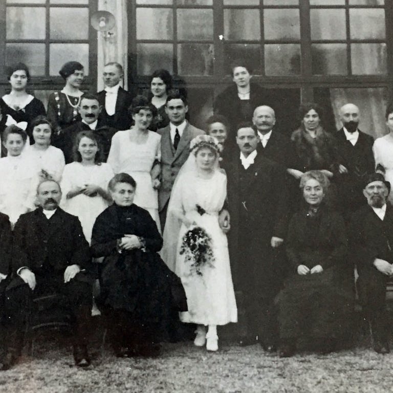 Eine Hochzeitsgesellschaft auf einem alten Schwarz-Weiß-Foto zeigt die Hochzeit von Simon Wolff und Karolina (Lina) Feiner