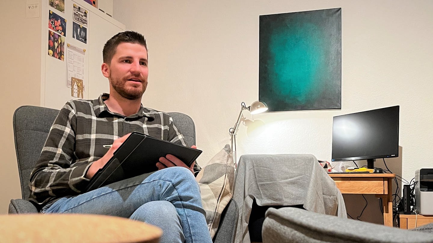 Der Psychotherapeut Marc Saxler-Netz sitzt auf einem Stuhl und macht sich Notizen - er betreut viele Patienten, die an den Folgen der Corona-Lockdowns leiden. (Foto: SWR)