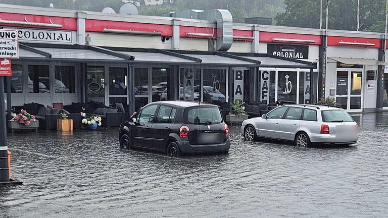 Zwei Autos stehen nach dem Starkregen auf dem überfluteten Parkplatz vor einem Supermarkt in Mudersbach.