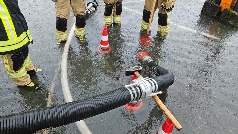 Feuerwehrleute stehen um einen Schlauch, der Wasser nach Starkregen in der Verbandsgemeinde Kirchen abpumpt