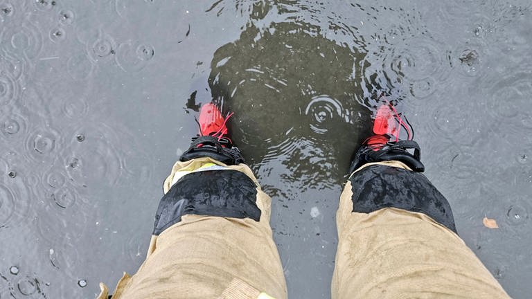 Ein Feuerwehrmann steht nach Starkregen in der Verbandsgemeinde Kirchen mit den Füssen im Wasser