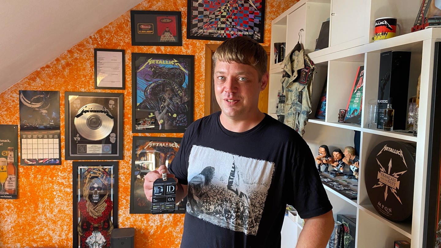 Ein Mann steht in einem Zimmer und hält einen VIP Pass für Metallica in der Hand (Foto: SWR)
