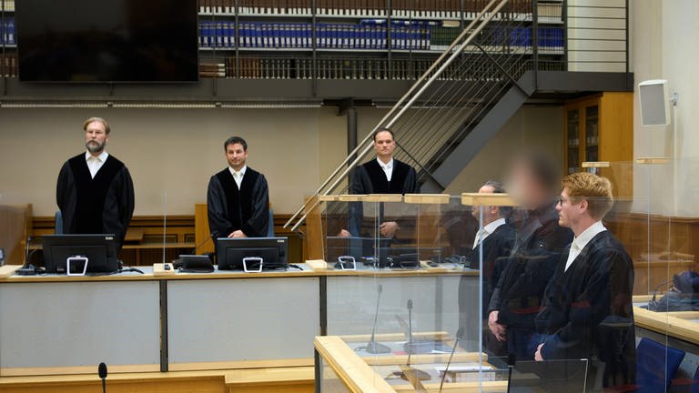 Der Angeklagte (2.v.r), dem vorgeworfen wird, 1991 einen Brandanschlag auf ein Asylbewerberheim in Saarlouis verübt zu haben, steht zu Prozessbeginn zwischen seinen Anwälten.
