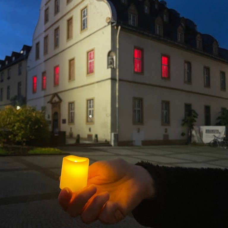 Eine Hand hält eine Kerze vor dem Bürresheimer Hof in Koblenz, der ehemaligen Synagoge. Am 9. November 2023 startete hier der Schweigemarsch zur Erinnerung an 85 Jahre Reichspogromnacht.