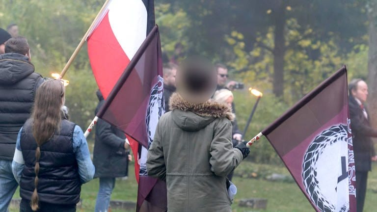 Drei Menschen halten eine Fahne bei einer rechtsextremen Veranstaltung in der Hand, darunter ein Junge in einer oliven Jacke. (Foto: Ronny Junghans)