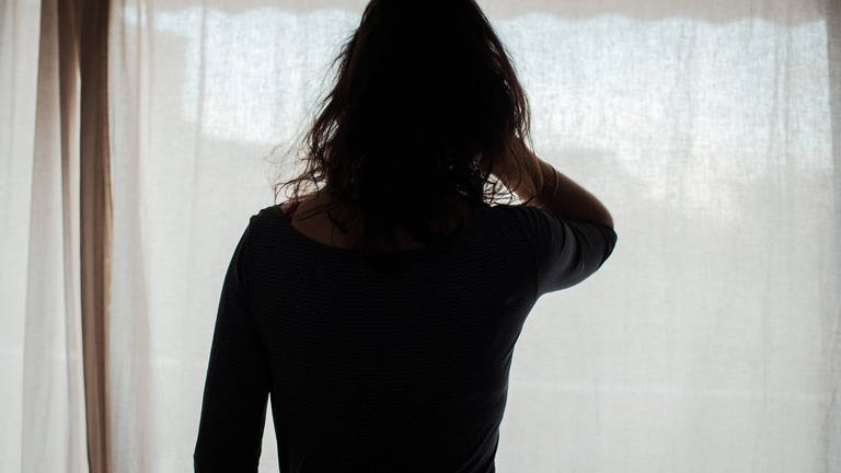 Eine Frau schaut aus einem Fenster mit Vorhang: Nach dem Mord an einer mutmaßlichen Prostituierten in Koblenz schlägt eine Beratungsstelle Alarm - die Gewalt gegen die Frauen nehme deutlich zu.