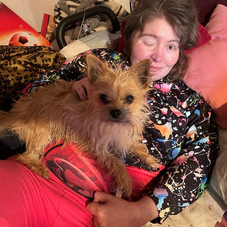 Heidi Wiese liegt auf ihrem Bett mit einem kleinen Hund im Arm