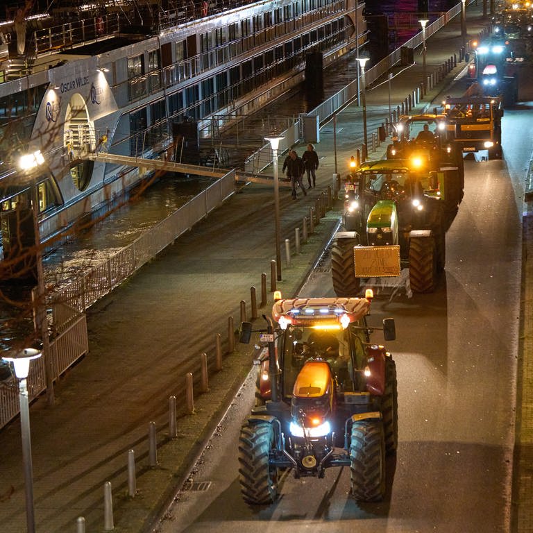 Mehrere Traktoren fahren im Dunkeln am Rhein in Koblenz entlang