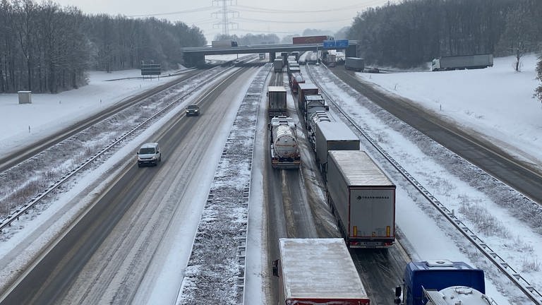 Auf der A61 ist wegen des starken Schneefalls ein langer Stau mit vielen Lastwagen.