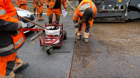 Ein Bauarbeiter pinselt die Kante zwischen dem fertigen und dem unfertigen Teil der Fahrbahn mit Klebemittel ein, damit im Anschluss asphaltiert werden kann. (Foto: SWR)