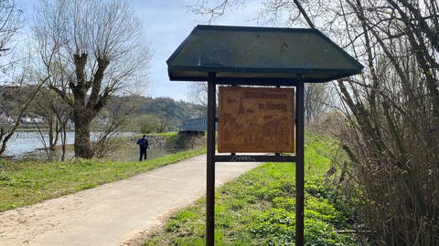 Ein altes Holzschild begrüßt die Radfahrer und Spaziergänger in Sinzig. Direkt dahinter sieht man die Ahrmündung, über die eine neue Brücke führt. (Foto: SWR)
