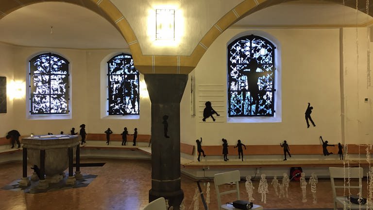 Schwarze Plexiglasfiguren von Erwachsenen und Kindern in der evangelischen Kirche in Winningen. Die Installation von Teresa Harb Diehl nutzt den ganzen Kirchenraum. 