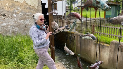 Die Künstlerin Michaela Klotz neben ihrem Kunstwerk mit Fischen aus Keramik am Flussufer in Antweiler: Sie will damit ein Zeichen gegen das Vergessen setzen