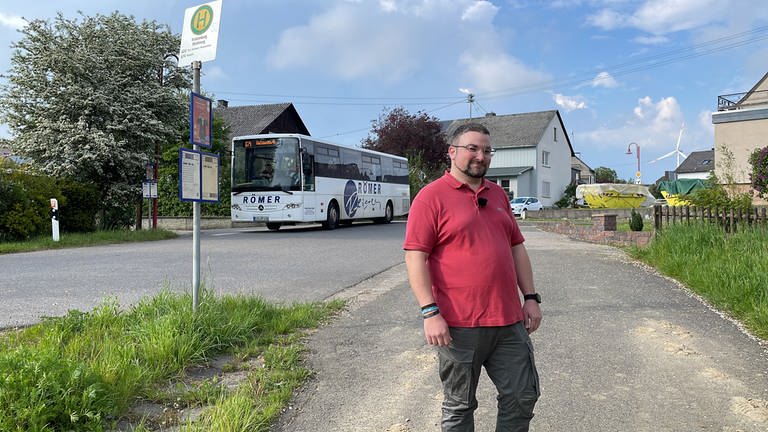 Tobias Stoffel steht an einer Bushaltestelle in Kratzenburg, im Hintergrund ein Bus.