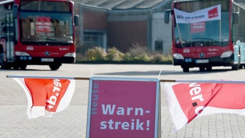 Ein "Warnstreik"-Schild" steht auf einem Platz, auf dem zwei Busse stehen. (Foto: dpa Bildfunk, picture alliance/dpa | Carsten Rehder)