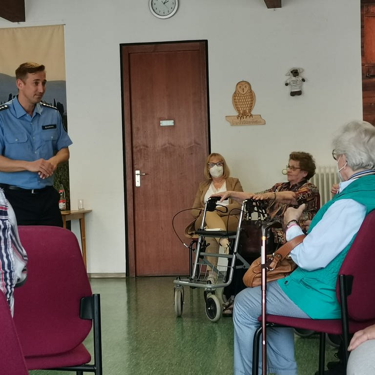 Ältere Menschen sitzen in einem Stuhlkreis. Vorne steht ein Polizist und spricht. (Foto: SWR)