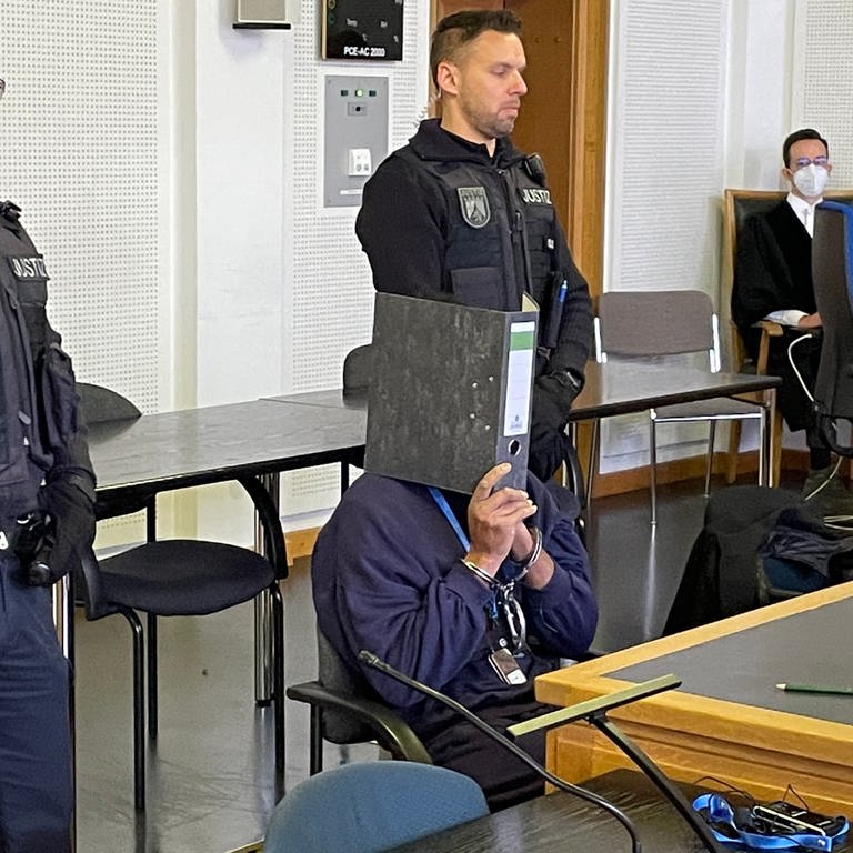 Der Angeklagte verbirgt sein Gesicht hinter einem Aktenordner (Foto: SWR)