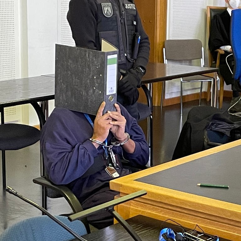 Der Angeklagte verbirgt sein Gesicht hinter einem Aktenordner (Foto: SWR)