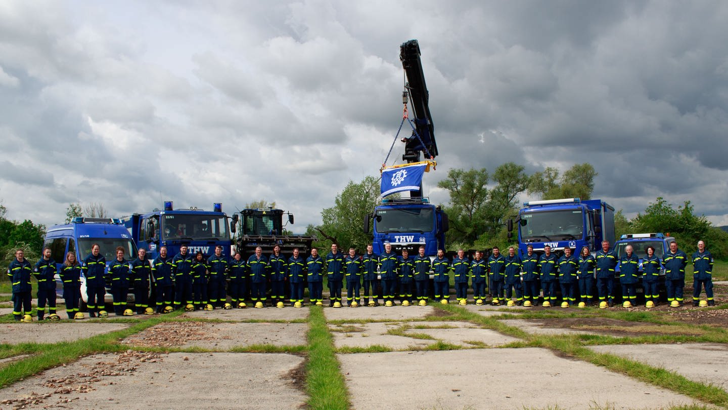 THW-Mitglieder stehen in dunkelblauen  Uniformen vor mehreren marineblauen Einsatzfahrzeugen, darunter einem Kran (Foto: THW Ortsverband Neustadt a.d.W.)