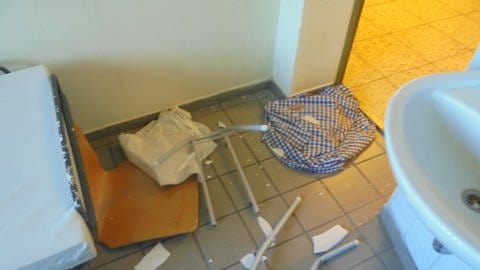 Eine Gefängniszelle, in der Stücke eines Stuhls und einer stertörten Klobrille auf dem Boden liegen. (Foto: JVA Frankenthal)