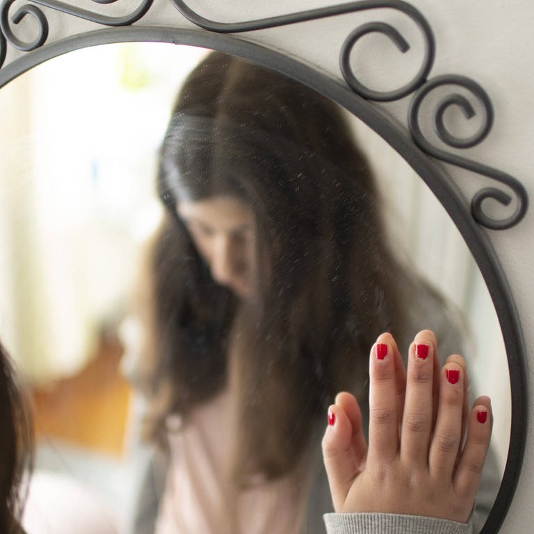 Mädchen mit gesenktem Blick vor Spiegel (Foto: IMAGO, photothek)