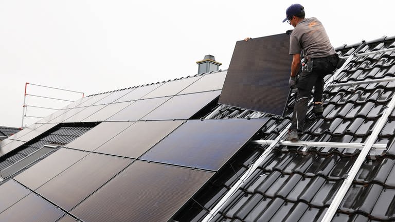Solaranlagen sind auf Neubauten in Neustadt an der Weinstraße künftig Pflicht - Bild von einem Handwerker, der ein Solarpanel auf einem Dach montiert (Foto: dpa Bildfunk, Oliver Berg)